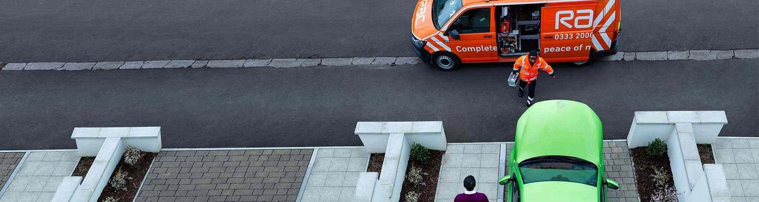 An RAC patrol parked outside a house and walking towards a car with its bonnet up on the drive